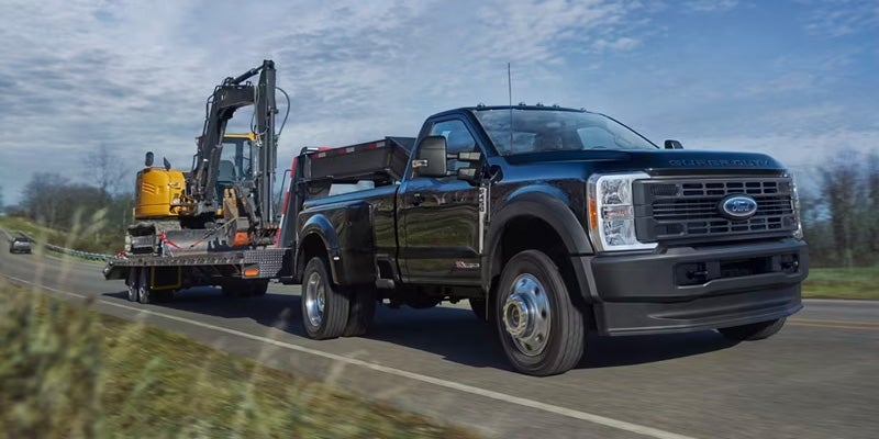 A black 2024 Ford F-250 driving down the highway and hauling an excavator behind