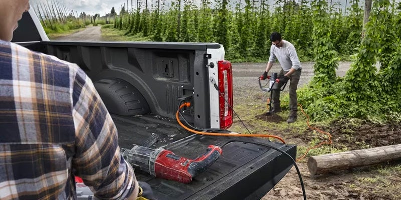 View of the bed on a white 2024 Ford F-250 Super Duty with the hatch down and a cord plugged in to the truck leading to a man using a power tool